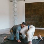 Two men practicing martial arts on floor mat in a minimalist gym setting.